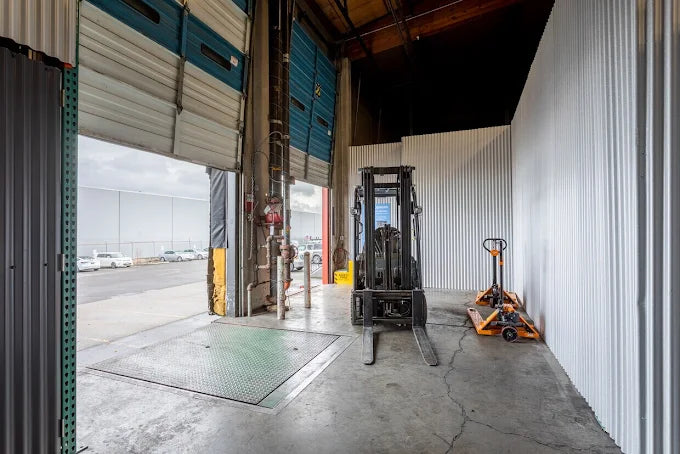 Front shot image of a forklift in a warehouse with two roll up doors opened.