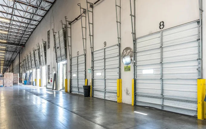 Sideways shot image of the inside of a warehouse with half the roll up doors opened and the other half closed.